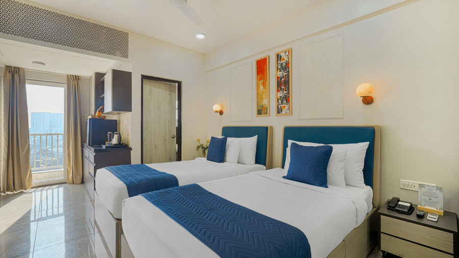 A hotel room at Urban Suites by BluSalzz, Jaipur, featuring with two single beds, bedspreads, pillows, wall arts, and a private balcony.