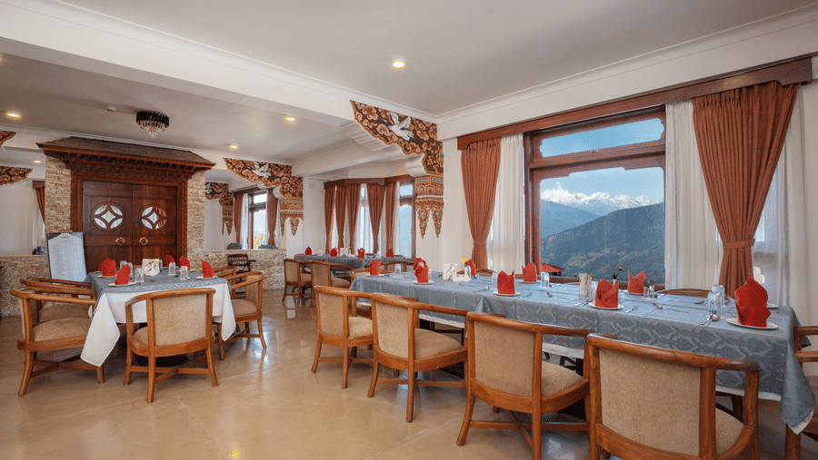 A dining room with multiple tables, chairs, and large windows with curtains at Summit Norbu Ghang - The Signature Collection, Gangtok.