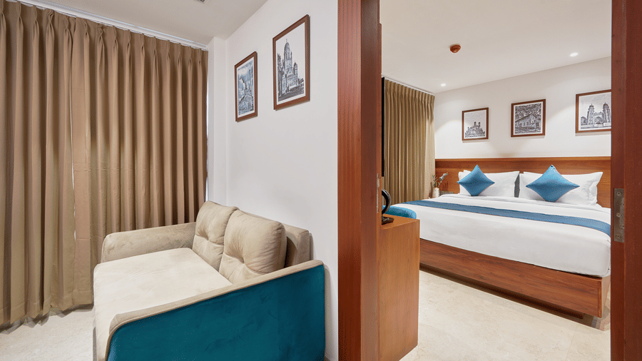 View of a suite at QWhite Crescent Luxury Hotel by Dimora Kochi with a connecting living area, teal sofa, king bed, and warm ambient lighting.
