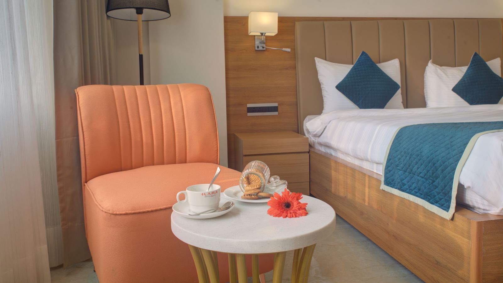 Cosy hotel room with a double bed, warm lighting, an orange armchair, and a small round table with refreshments at Ilara Hotels & Spa.