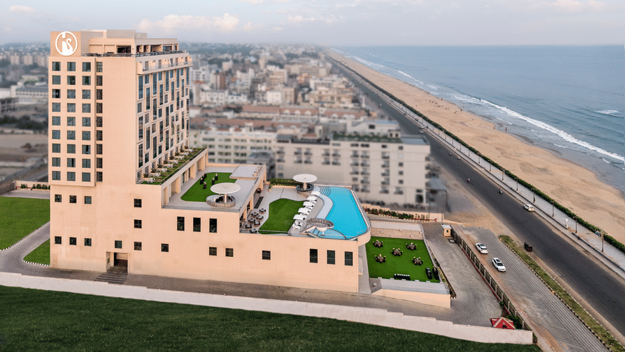 The well-lit facade of Swosti Premium Beach Resorts, Puri, featuring a curved infinity pool on a terrace facing the road, and sea infront.