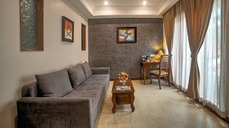 Spacious suite living room with plush grey sofa and natural light from full-length curtains at Ilara Hotels & Spa, OMR, Chennai