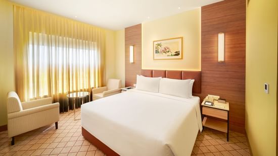 A warm-toned hotel room featuring a large bed, a desk area, and artwork on the walls | Suite | Sarovar Portico, Sriperumbudur
