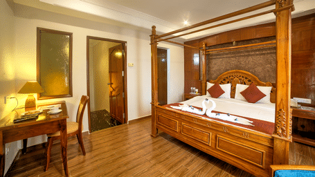 Luxurious four-poster bed with classic wooden furniture and warm ambient lighting at Ilara Hotels & Spa, OMR, Chennai