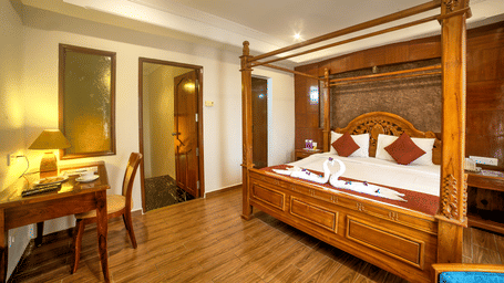Luxurious four-poster bed with classic wooden furniture and warm ambient lighting at Ilara Hotels & Spa, OMR, Chennai