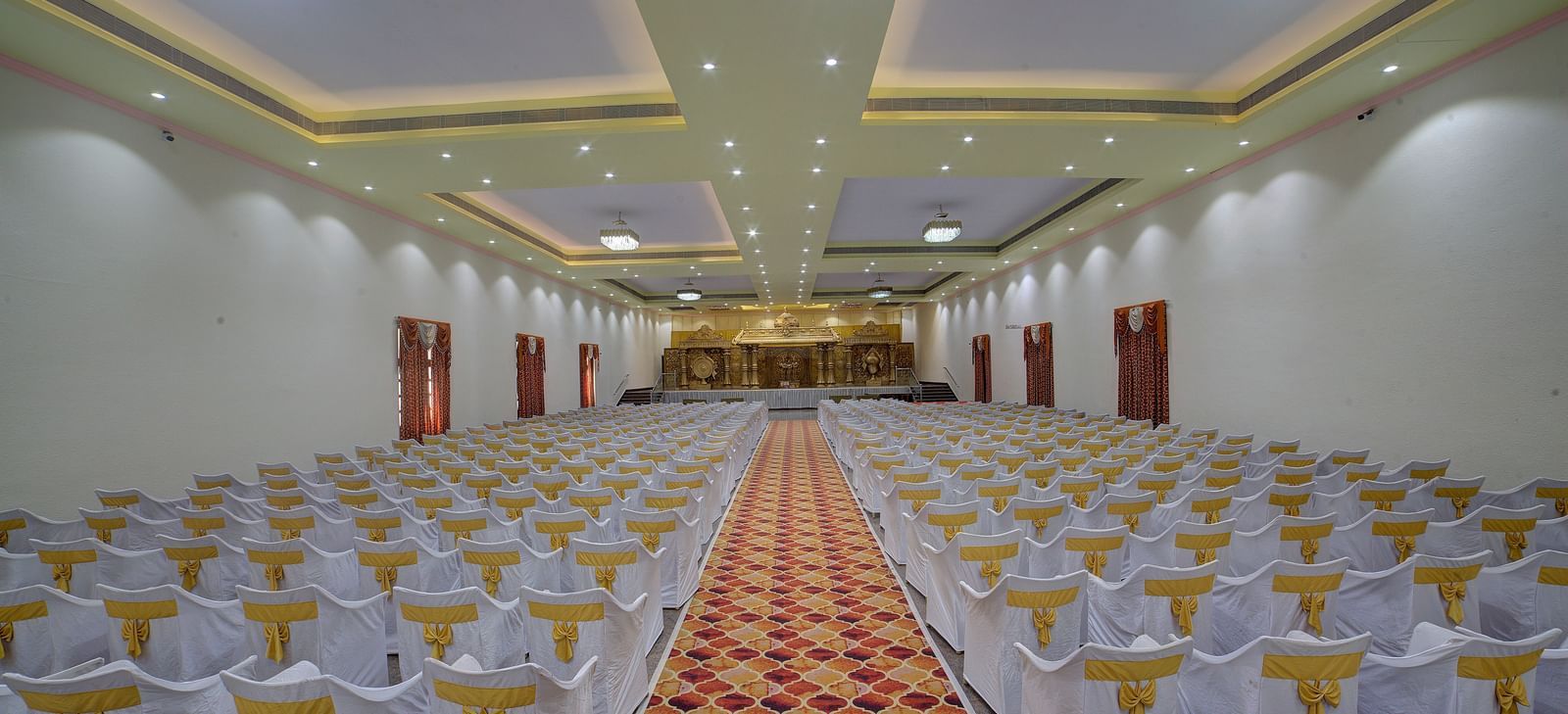Indoor banquet hall with rows of white chairs and a central aisle at Kailash Conventions ECR.