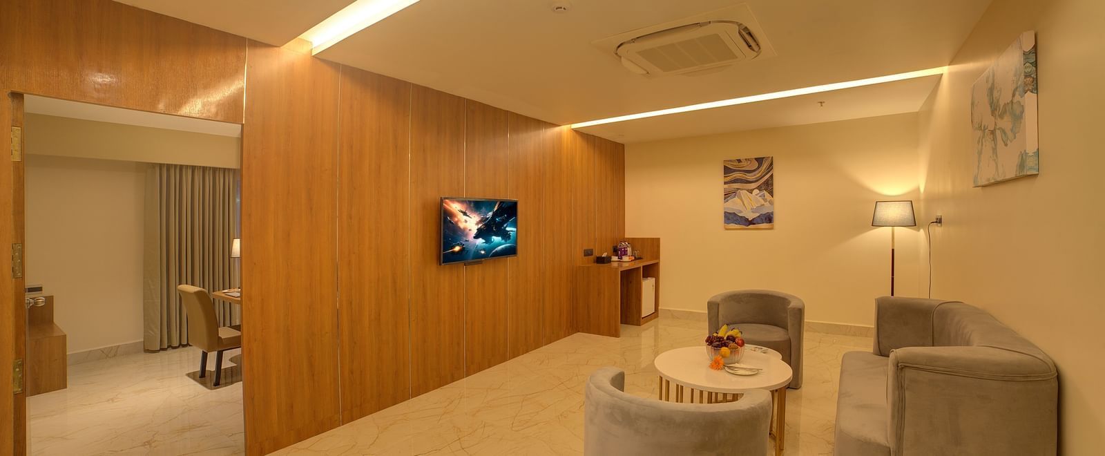 A separate living room featuring a grey coloured couch set with a wall mounted television on wooden panels at the Executive Suite of Ilara Hotels & Spa, Tada.
