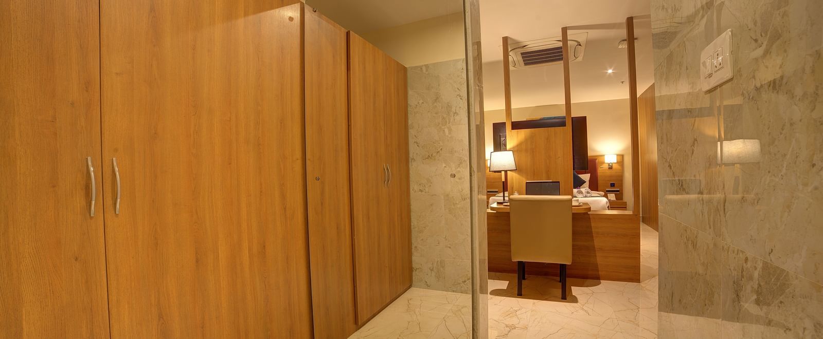 A full length mirror besides the wooden wardrobe at the Executive Suite with a doorway going leading to the bedroom at Ilara Hotels & Spa, Tada.