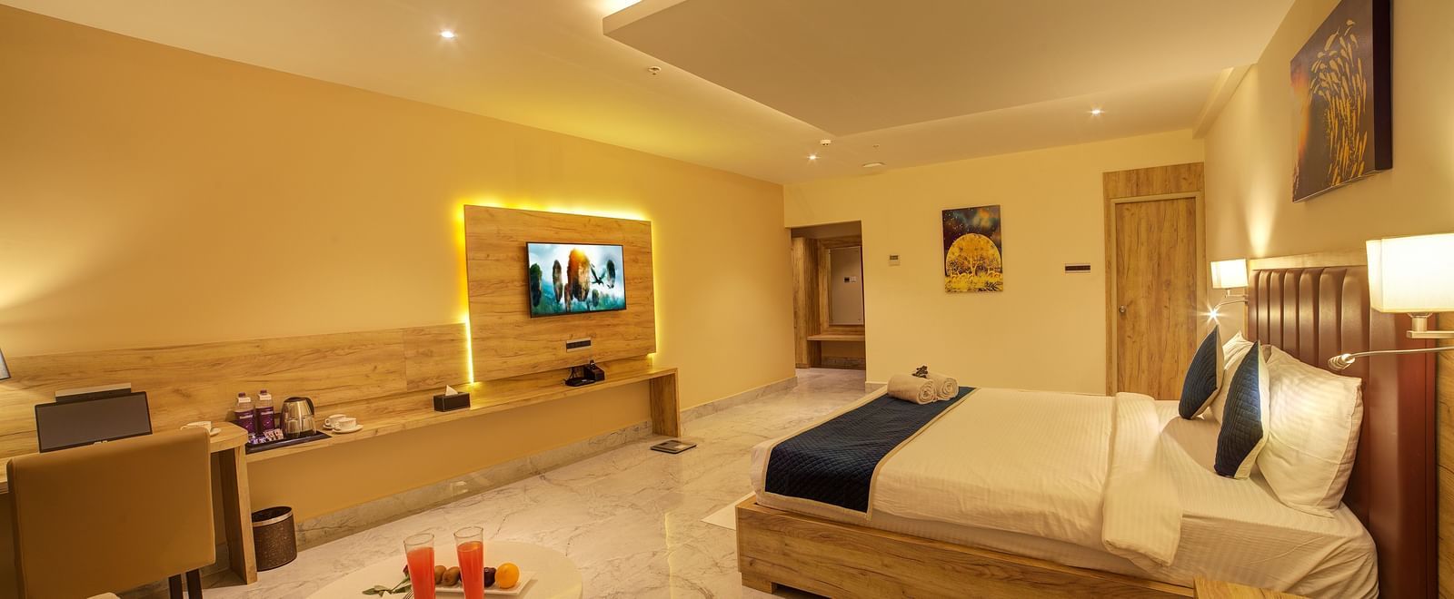 A wide angle shot of the Junior Suite with a coffee table along with a double bed and a wall mounted television and a work station.