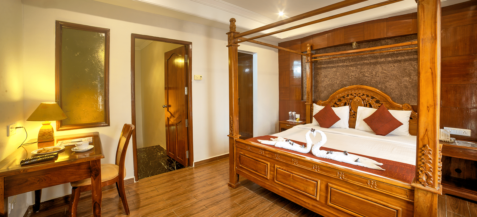 Luxurious four-poster bed with classic wooden furniture and warm ambient lighting at Ilara Hotels & Spa, OMR, Chennai