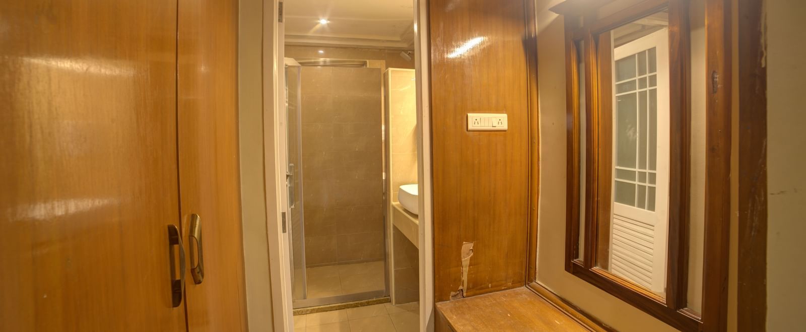 Changing area with wooden panelled wardrobe and enclosed glass door at Ilara Hotels & Spa, OMR, Chennai