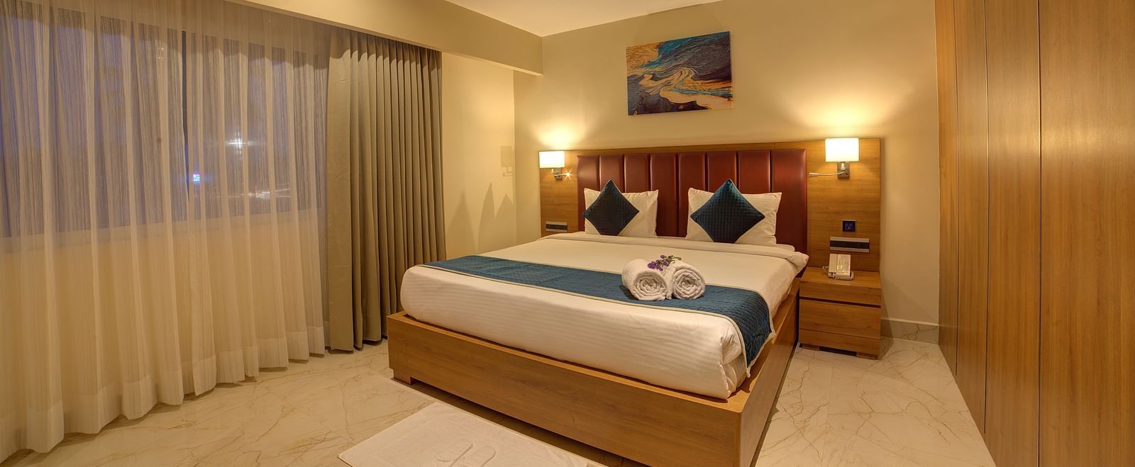 A close up shot of a plush double bed with two bed side lamps in the Executive Suite and a white rug in front of it at Ilara Hotels & Spa, Tada.