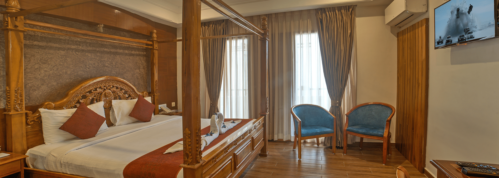 Elegant wooden bed with twin chairs and ambient lighting in a spacious room at Ilara Hotels & Spa, OMR, Chennai