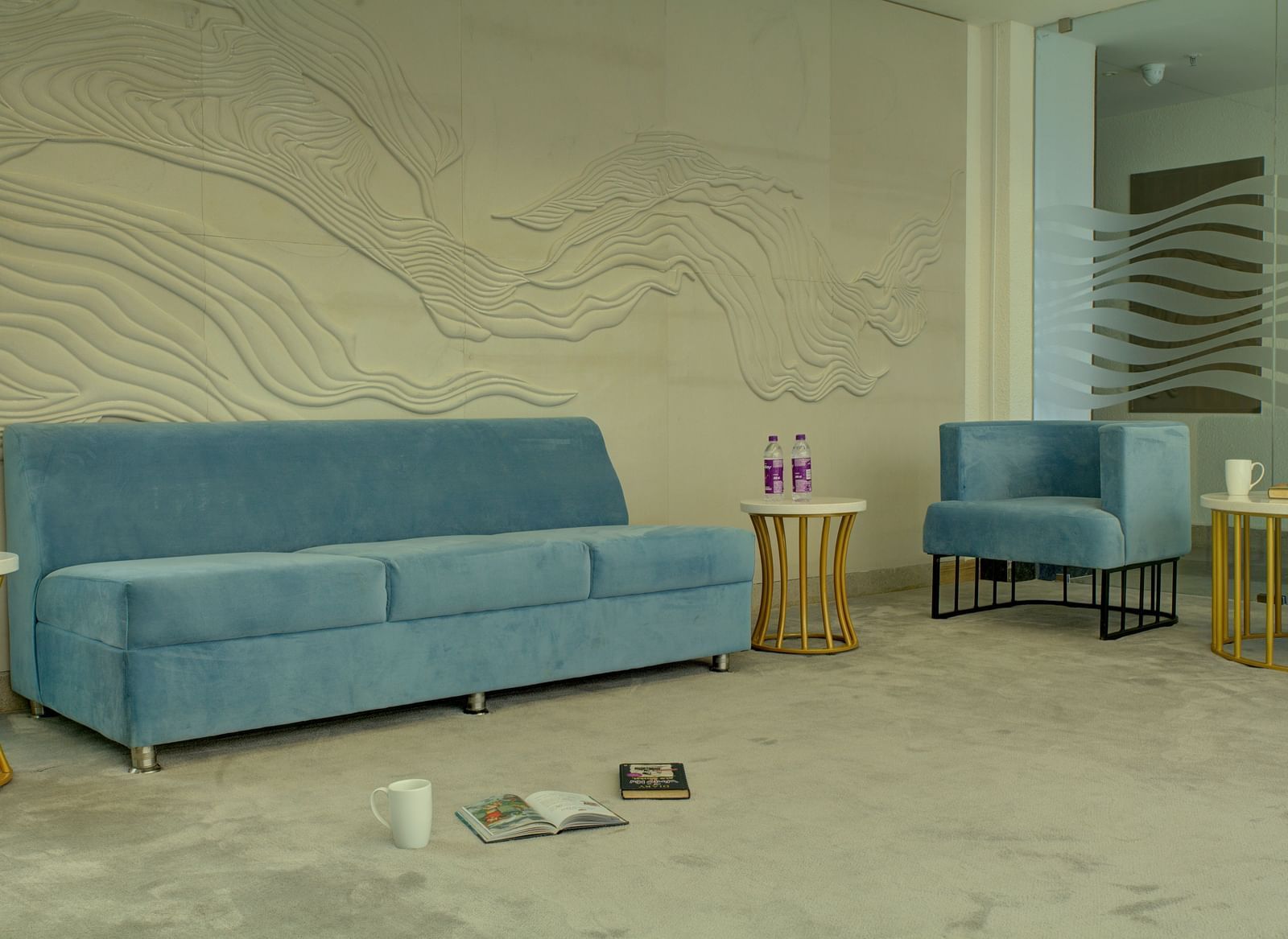 A plush blue couch in the lounge area with a few books kept on the floor at Ilara Hotels & Spa, Tada.