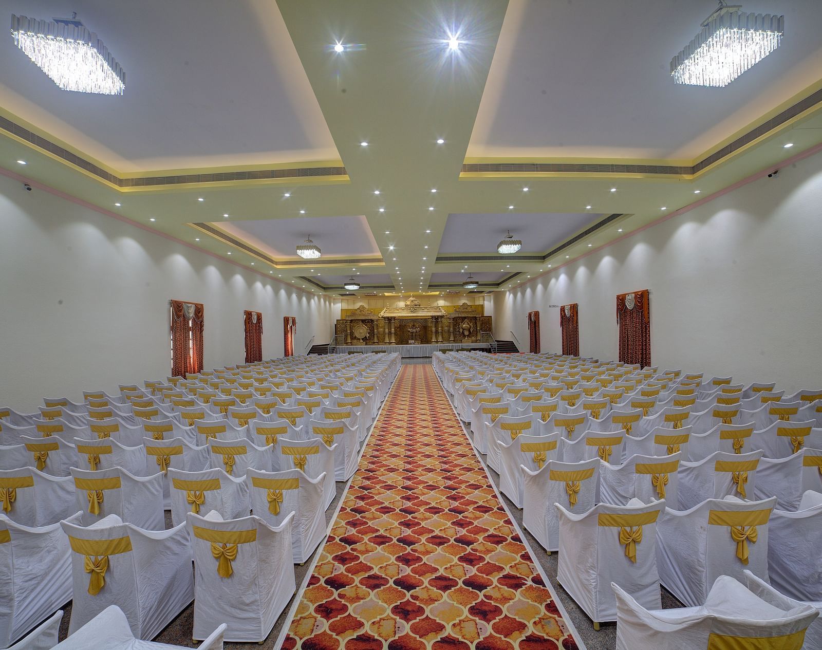 Indoor banquet hall with rows of white chairs and a central aisle at Kailash Conventions ECR.