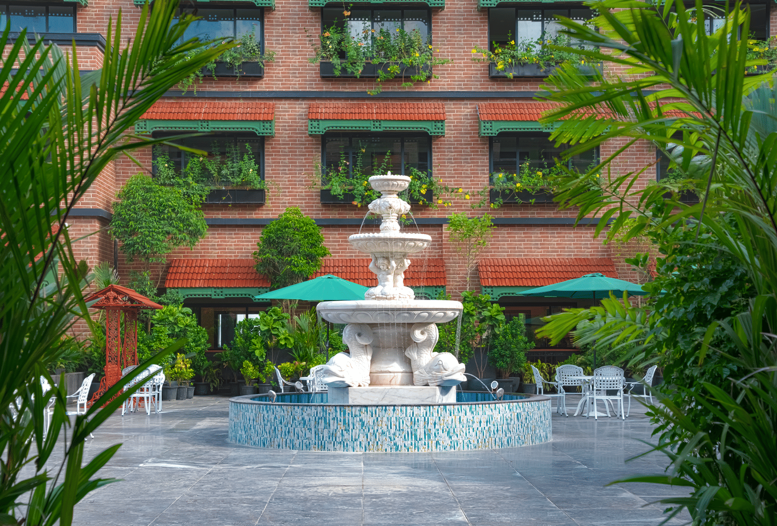 A garden courtyard with a decorative stone fountain surrounded by greenery, manicured plants and pathways, set against the building’s exterior at MAYFAIR Bay Resort, Paradeep.