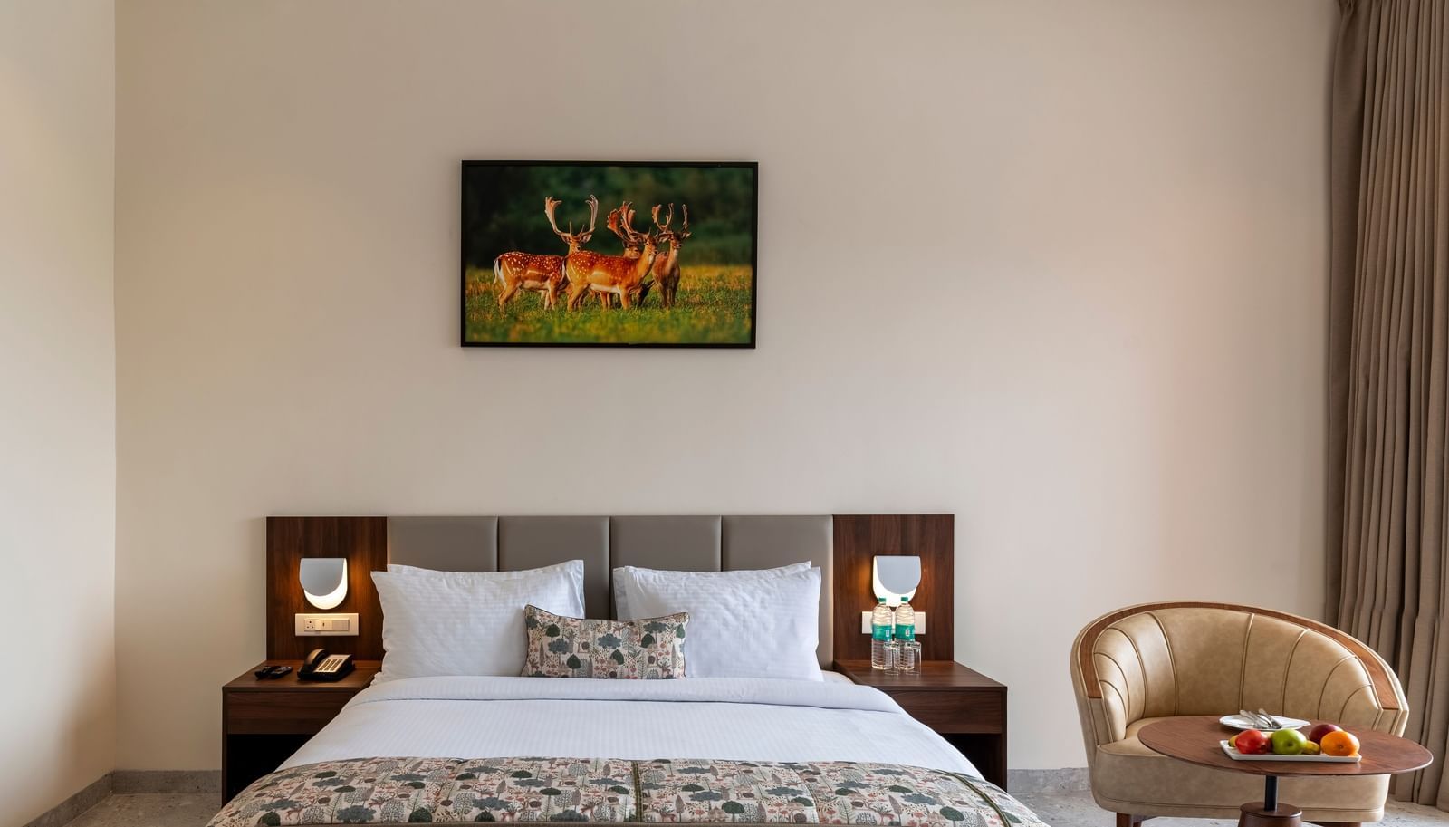 A bright bedroom at Osian Valley Resort & Spa with a double bed, bedside tables, and a painting of deer hanging above the headboard.