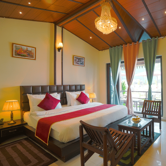 A neatly arranged room with a big bed, 2 wooden chairs on either side of a coffee table, a chandelier and full length curtains | Sol Glow Resort, Nainital