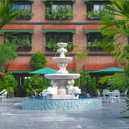 A lawn courtyard with a decorative stone fountain surrounded by greenery, manicured plants and pathways, set against the building’s exterior at MAYFAIR Bay Resort, Paradeep.