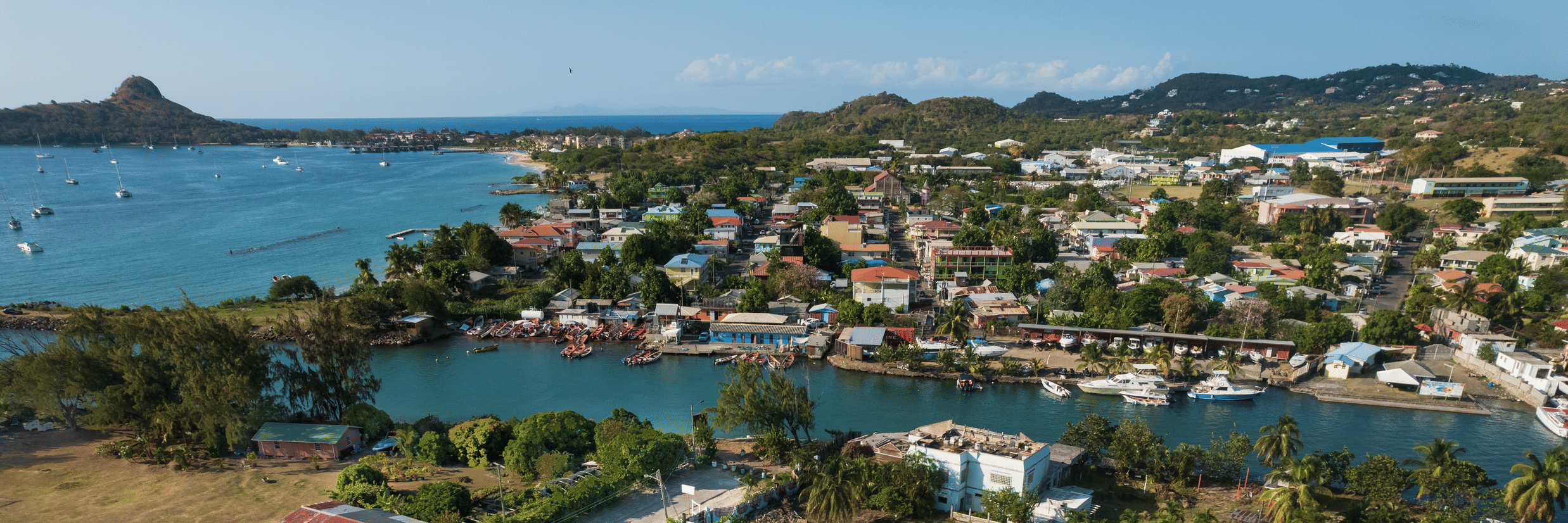 An aerial view the Soco House's facade highlighting the swimming pool, tennis court, and nearby waterfront, surrounded by lush greenery and a coastal town in St. Lucia.