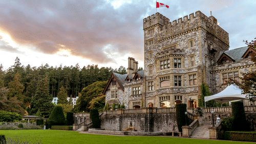 An image of a castle with lush greenery and trees around while having a beautiful sky in the background