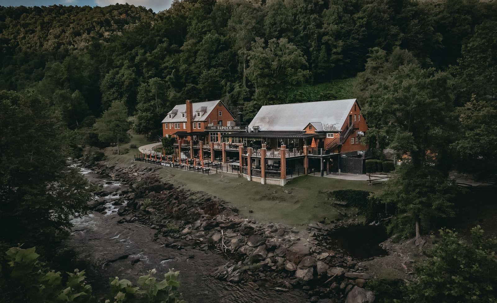 Cottages at the Historic Tapoco Lodge set amidst the tall trees, steep hills, and a stream is running in front of the property.