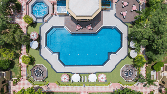 An aerial view of the expansive outdoor swimming pool with a nicely manicured garden surrounding it at the Heritage Village Resorts & Spa, Manesar, one of the best weekend getaways from Gurgaon.
