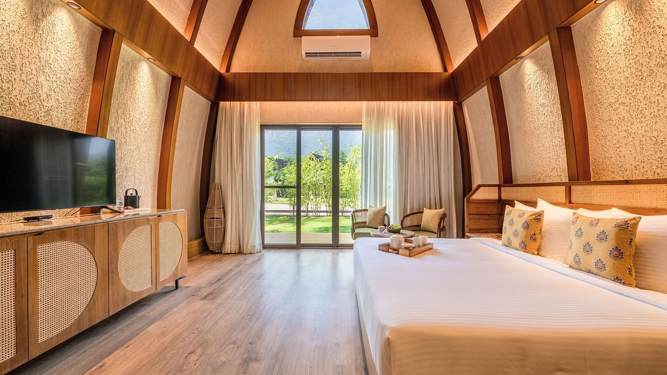 An image of attic style bedroom with a king size bed, a flat TV screen, and a large window from where the outdoor scenes can be enjoyed - Ananta Spa and Resort, Ajabgarh