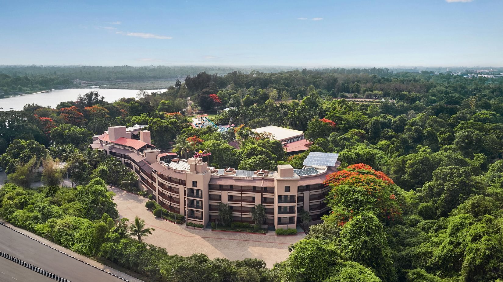 DGV Resort by Treat, Silvassa nestled in dense greenery, featuring a curved main building, waterpark, and nearby river under a clear blue sky.