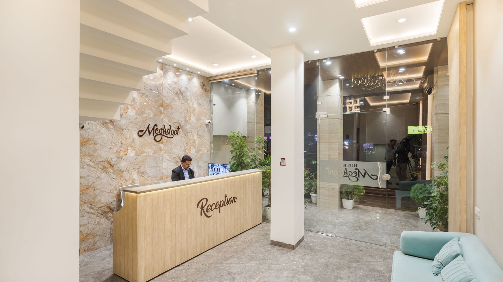 Modern hotel reception area with a wooden front desk, receptionist, stylish ceiling lights, and glass entrance at Morya Hotels.