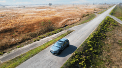 A far out view of a car driving in the middle of the road with greenery around