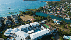 An aeriel view of The Soco House and the nearby waterfront surrounded with lush greenery and the coastal landscape, and a scenic hill and the sea meeting the sky on the horizon at the backdrop.