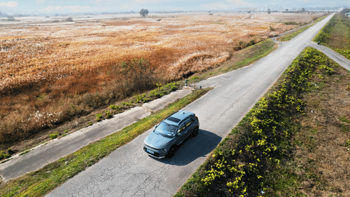 A far out view of a car driving in the middle of the road with greenery around