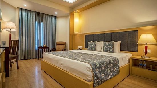 Standard bedroom with a double bed, lamps, chairs, and curtains at Golden Tulip, Udaipur.