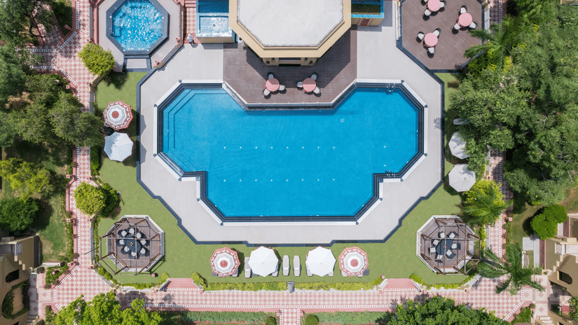 An aerial view of the expansive outdoor swimming pool with a nicely manicured garden surrounding it at the Heritage Village Resorts & Spa, Manesar, one of the best weekend getaways from Gurgaon.
