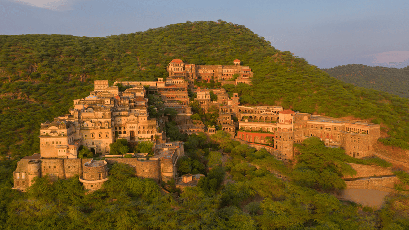 Neemrana Fort Palace surrounded by lush greenery and green hills. The property is huge and spread across the land with several sections.
