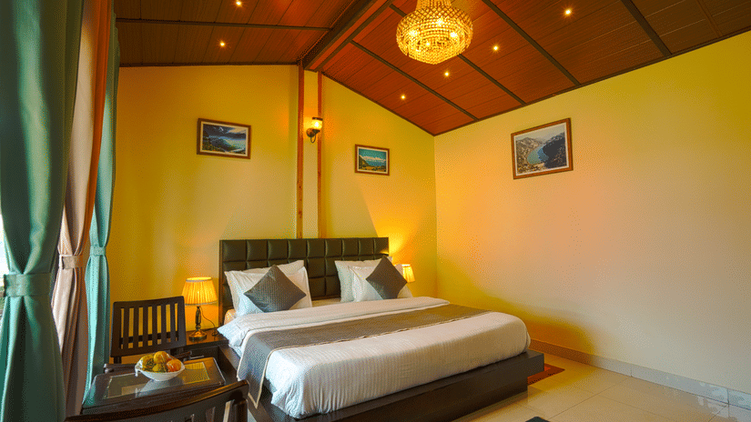 A neatly arranged room with a king bed with cushions, two chairs and a coffee table, a large chandelier, alongside 3 wall hanged paintings |Sol Glow Resort, Nainital