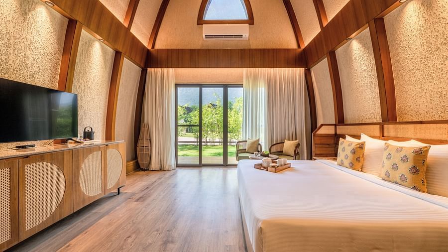 An image of attic style bedroom with a king size bed, a flat TV screen, and a large window from where the outdoor scenes can be enjoyed