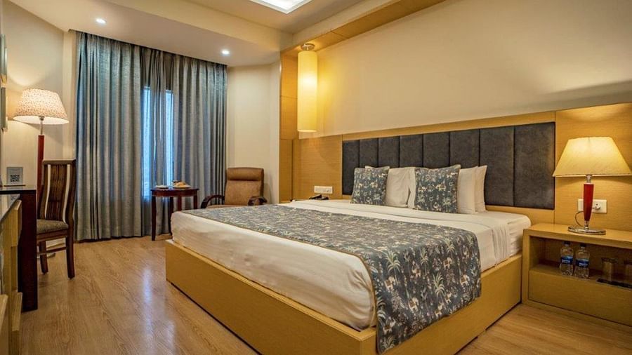Standard bedroom with a double bed, lamps, chairs, and curtains at Golden Tulip, Udaipur.