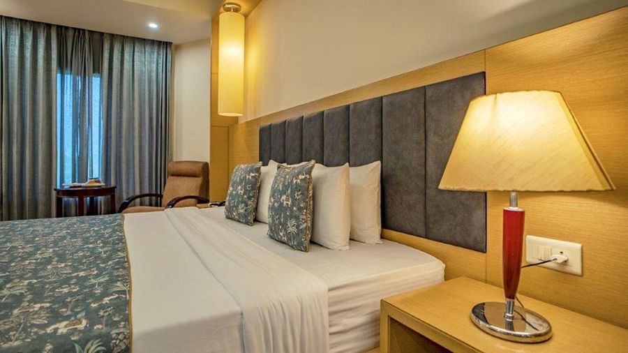 Warmly lit room with bed, side lamp, and full-length curtains at Golden Tulip, Udaipur.