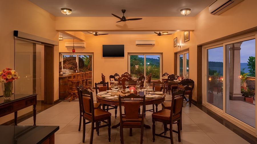 A dimly lit dining area with wooden chairs placed around dining tables - Highland Sarovar Portico, Sindhudurg