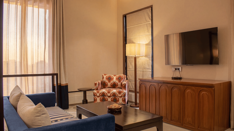 A bedroom lounge setup with a blue sofa, armchair, coffee table, television unit, and floor lamp at The Sierra - By The Lake.