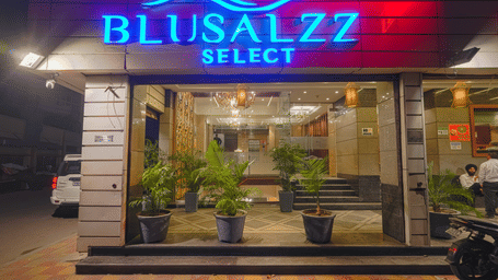 The ground-level entrance of the hotel at night, illuminated by a bright blue and red neon sign at BluSalzz Select City Centre, Amritsar.