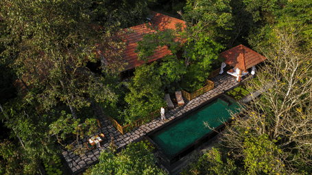 Aerial of Estate Chadachil with tiled roofs, a stone terrace, a dark-tiled pool and a curtained pavilion set in forest at Earthitects Holiday Experiences.