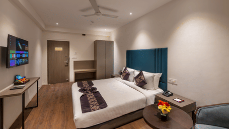  Lords Eco Inn bedroom with a large bed, a headboard, a ceiling fan, a small circular table, and a TV on the wall.