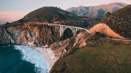 Stunning aerial shot of Bixby Creek Bridge in California during sunset, capturing the rugged coastline and turquoise ocean