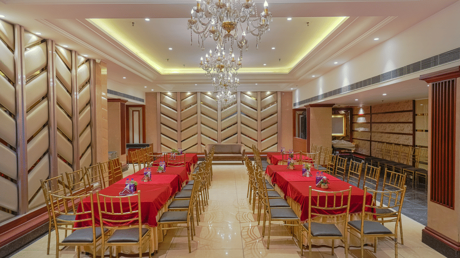 A wide view of the elegant private dining room, set up with multiple rectangular tables and an ornate chandelier at BluSalzz Select City Centre, Amritsar.