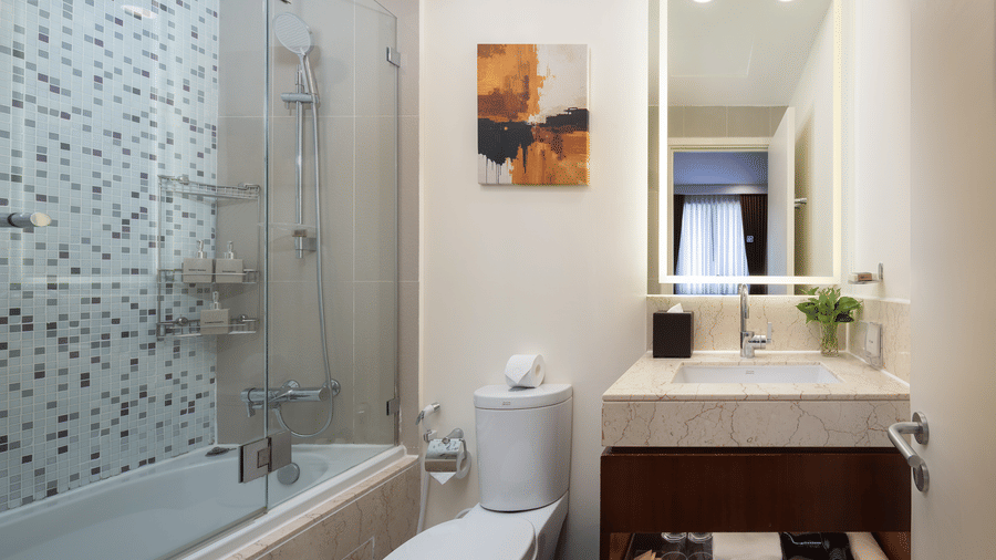 Bathroom of the Studio with Workspace at Central Mansions, Phnom Penh with a bathtub, glass shower partition, vanity, and modern amenities.