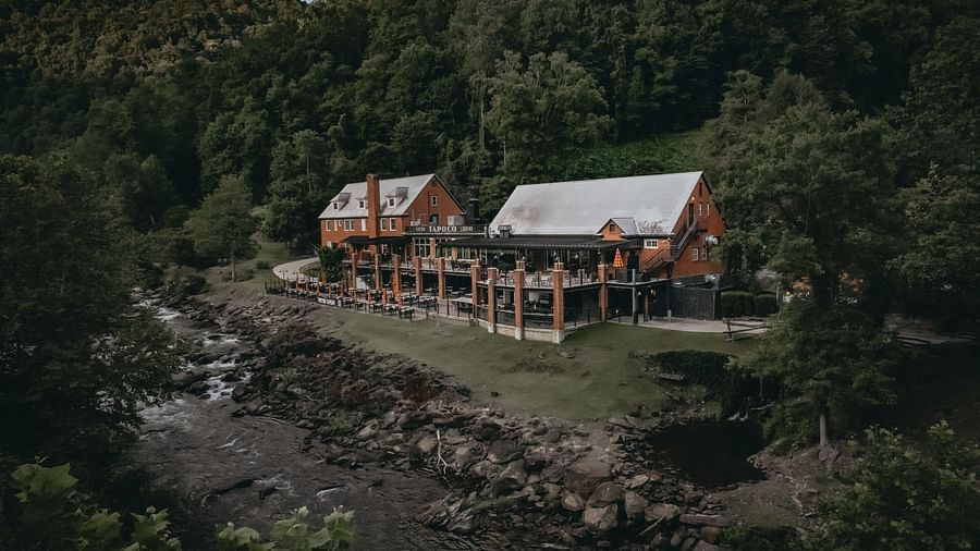 Cottages at the Historic Tapoco Lodge set amidst the tall trees, steep hills, and a stream is running in front of the property.