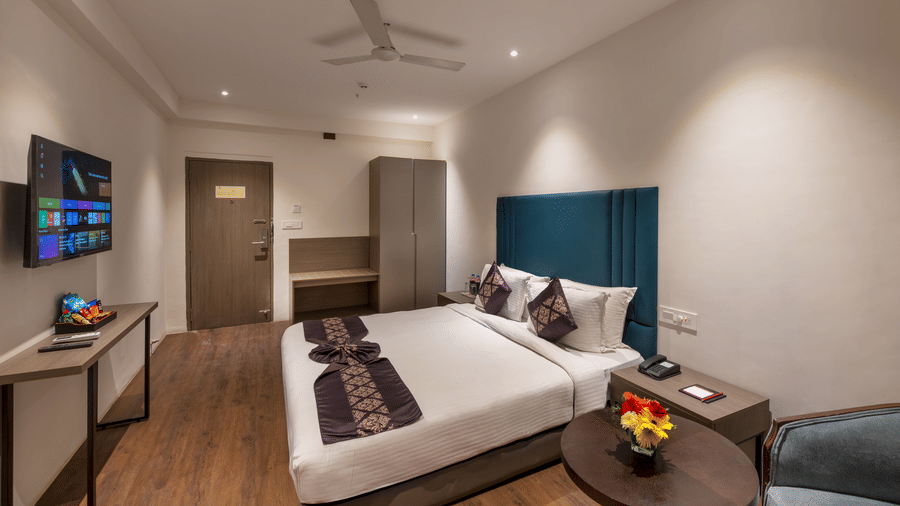  Lords Eco Inn bedroom with a large bed, a headboard, a ceiling fan, a small circular table, and a TV on the wall.